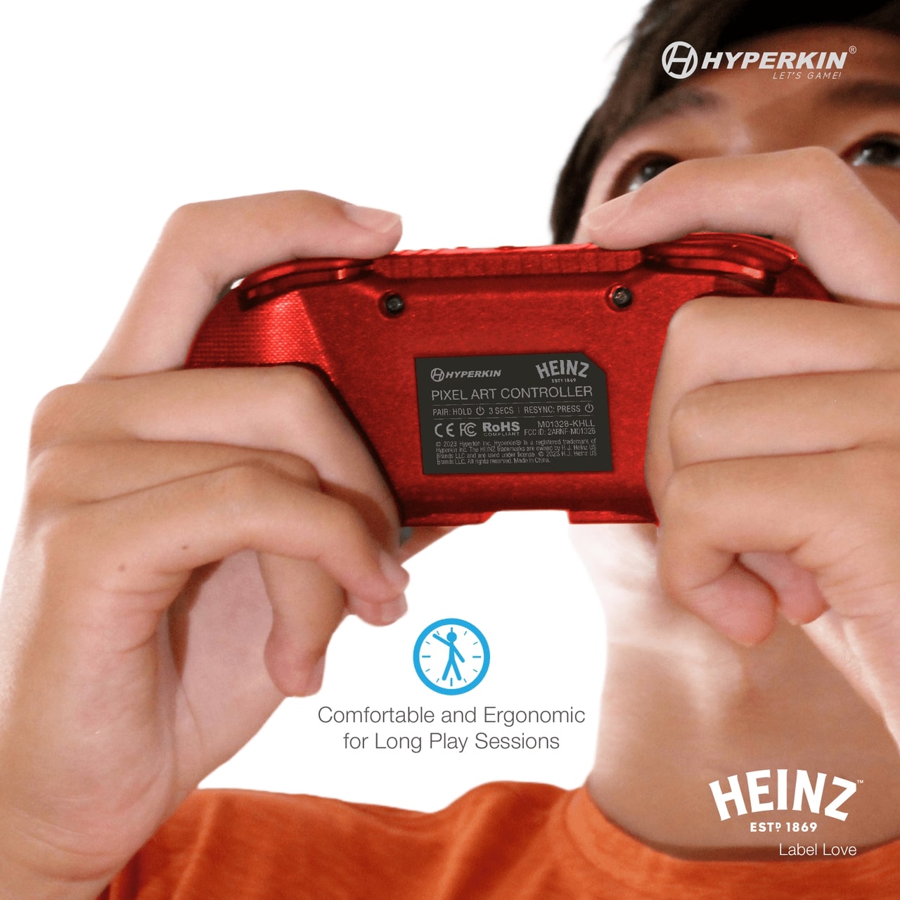 Red Hyperkin Heinz Pixel Art Bluetooth controller held close to face, showing back label with certifications and model info. Includes Hyperkin and Heinz logos, and text highlighting ergonomic comfort for long gaming sessions.