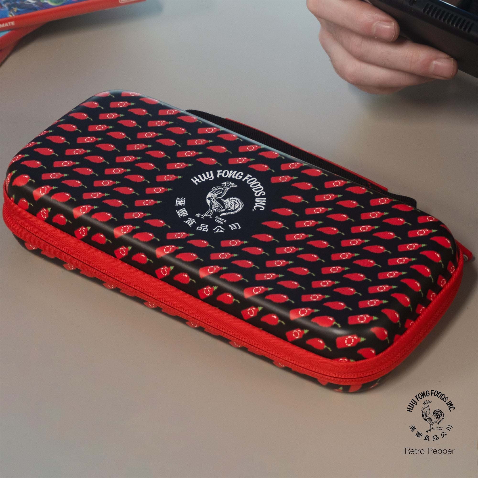Black and red zippered carrying case with chili pepper pattern and Huy Fong Foods rooster logo, placed on a light surface.