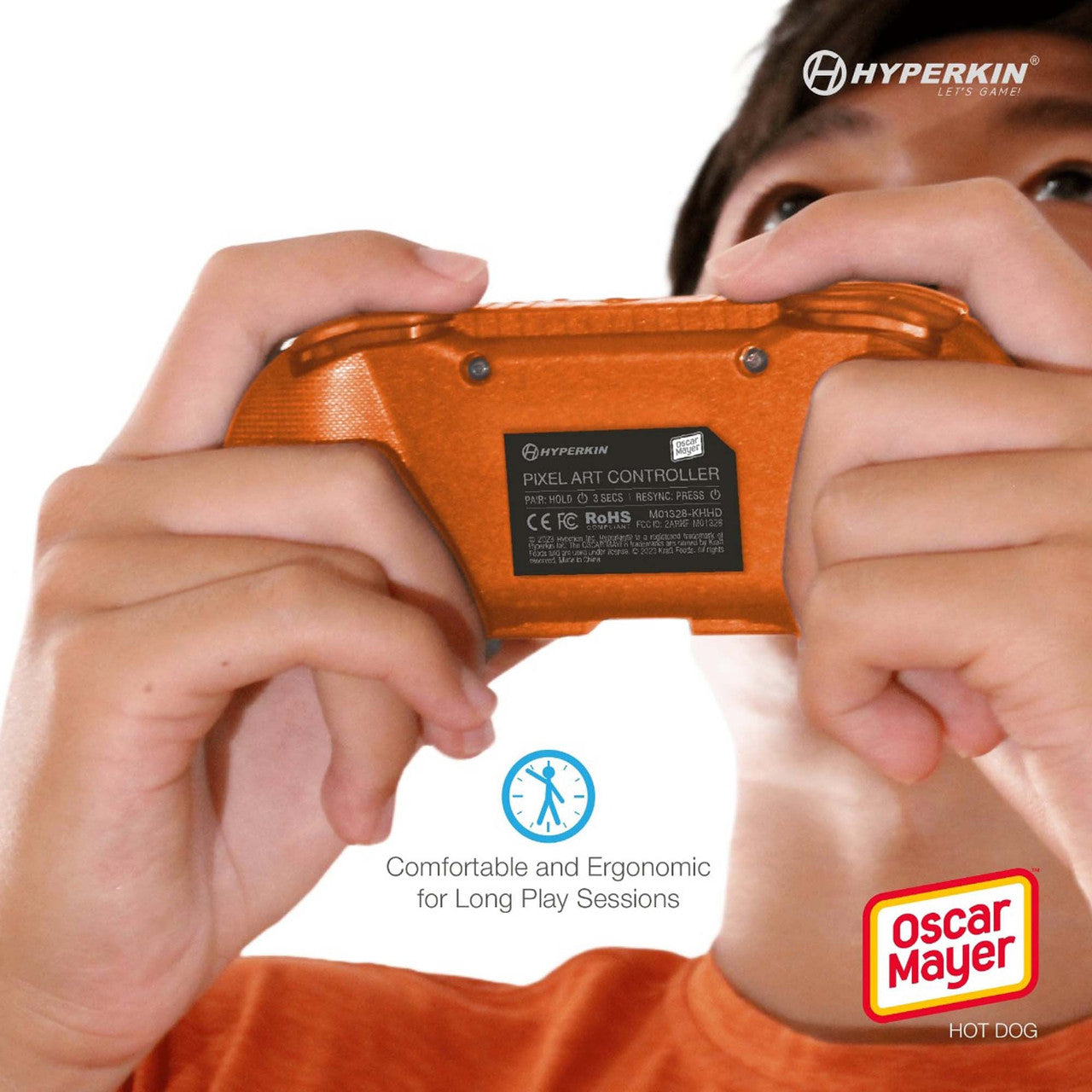 Person holding orange Hyperkin Pixel Art Controller with Oscar Mayer Hot Dog branding, showing back label with technical specs. Includes ergonomic comfort icon and Hyperkin slogan.